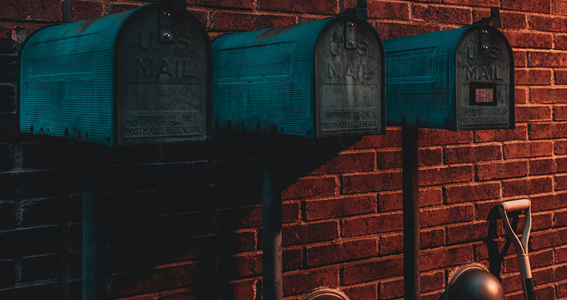 Three green mailboxes against a brick wall in low light